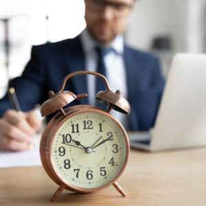 a businessman working on a computer behind a clock with bells on it