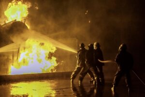 Firefighters extinguishing an industrial fire at the fire station holding on to the hose spraying the fire at a storage tank.