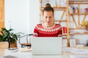 Concentrated female freelancer sitting at table and browsing laptop while working on remote project in cozy workplace at home