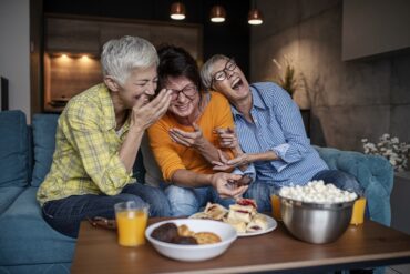 Three senior women having wonderful time while eating sweet and salty snacks in the living room