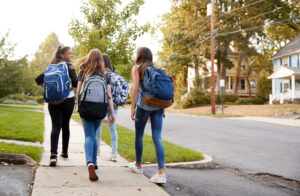 From the back you see a group of teen girls walking along a suburban street.
