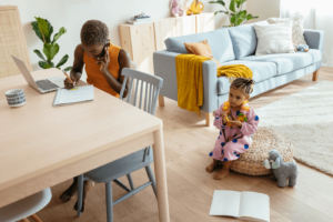 High angle of African American woman talking on smartphone and making notes while sitting at table near adorable mixed race girl at home