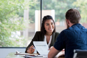 Broker at a desk meeting with consumer and reviewing a policy