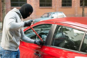 Thief In Hooded Jacket And Balaclava Opening Car's Door With Crowbar