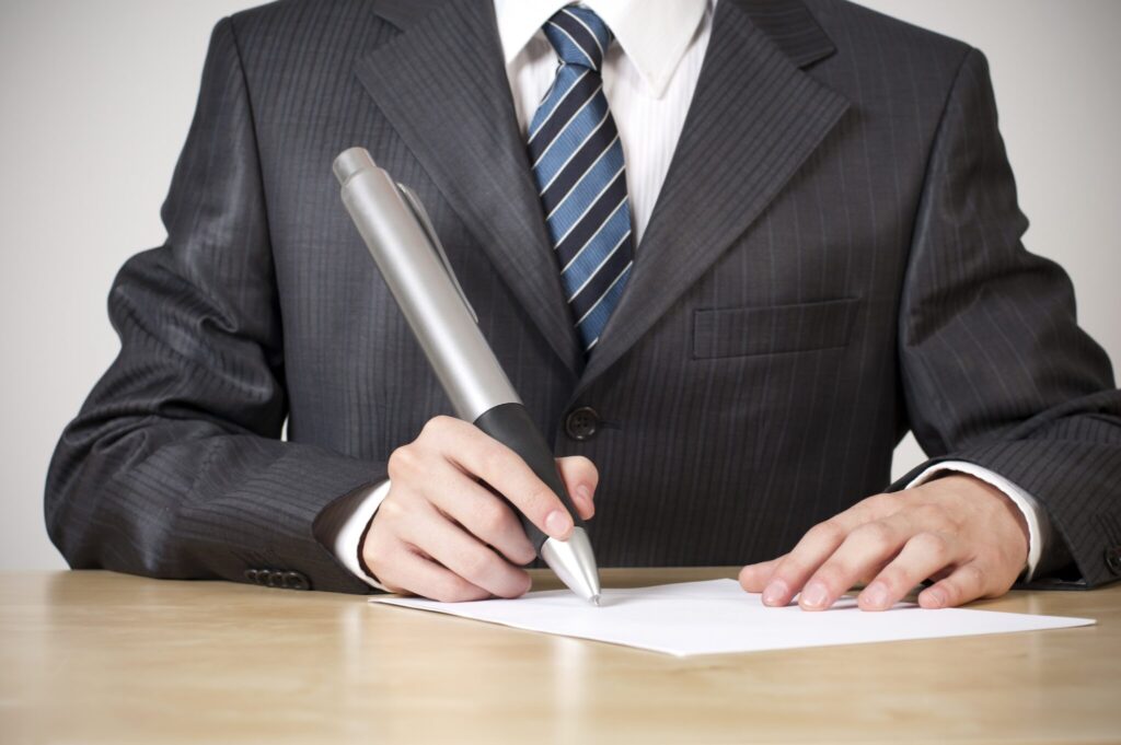 Business signing a piece of paper at a desk with an oversized pen