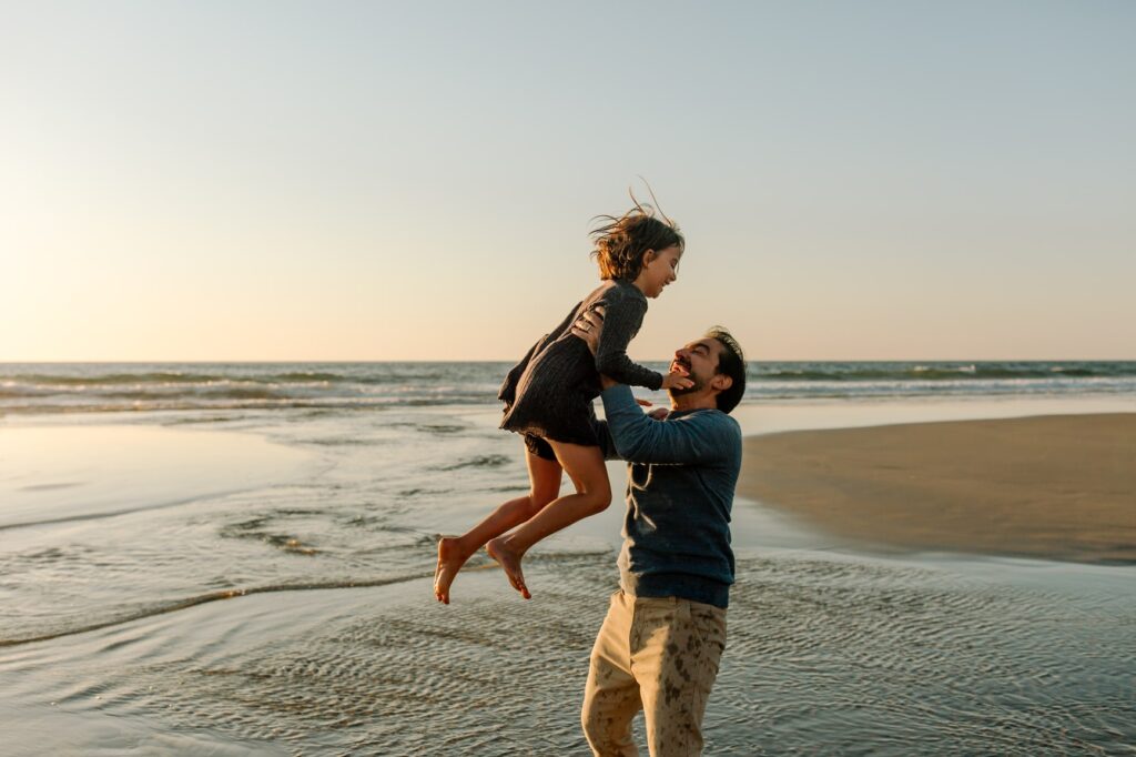 Close up of happy dad with beard holding laughing girl while standing in water.