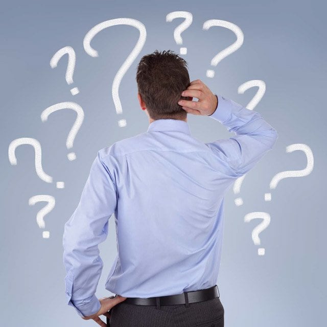 A man confused and looking at a set of question marks on a wall