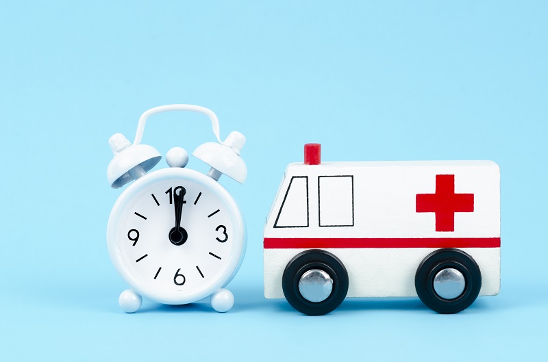 Ambulance toy wooden block and alarm clock on blue background. Emergency healthcare medical concept.