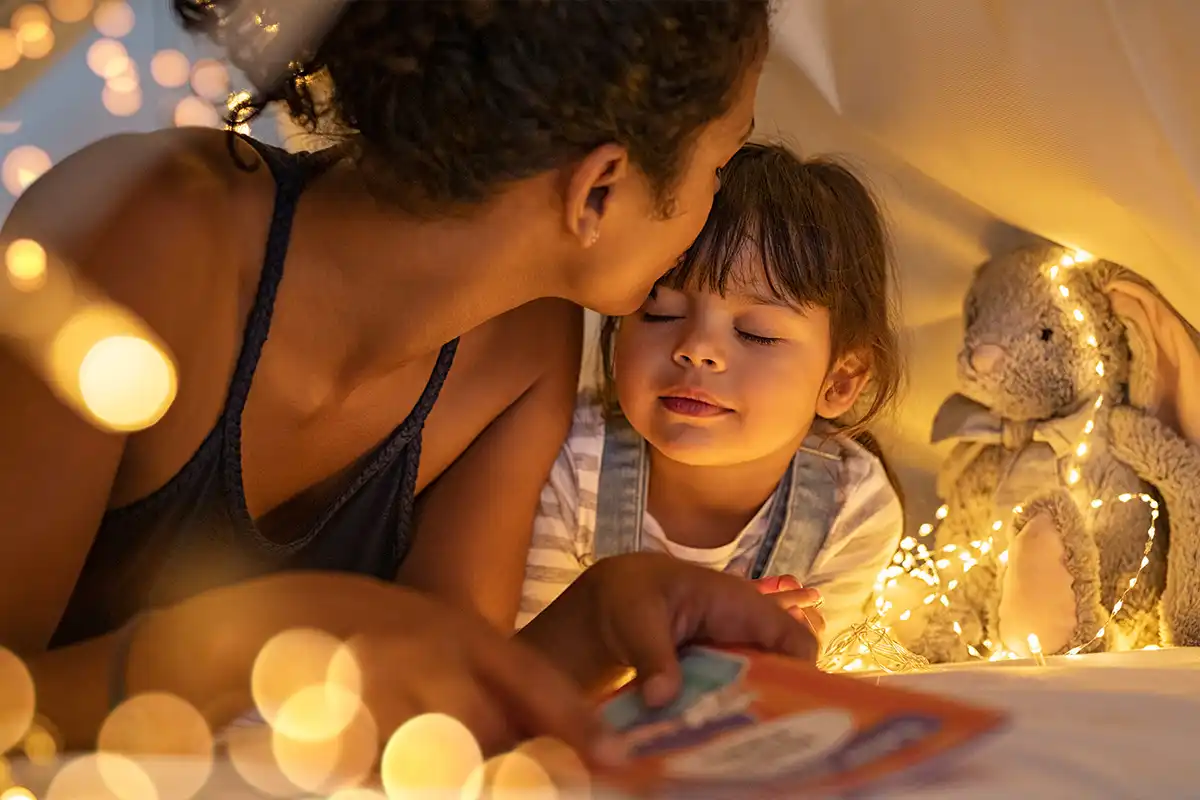 Loving ethnic mother kissing daughter in cozy hut