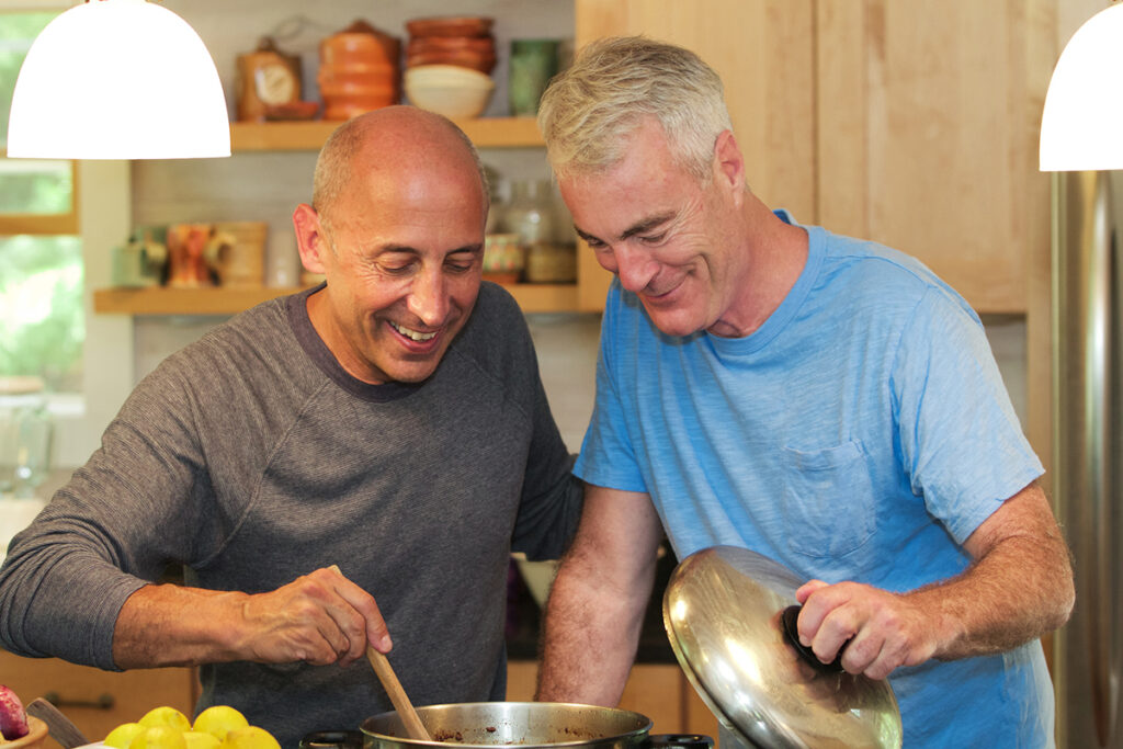Senior gay male couple at home cooking together