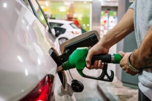 Unrecognizable male putting fuel dispenser in tank while refueling vehicle on self service gas station.