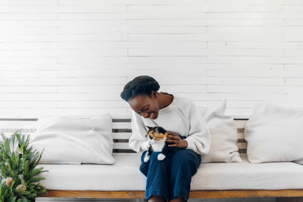 Beautiful young black woman sitting on couch and cuddling her cat