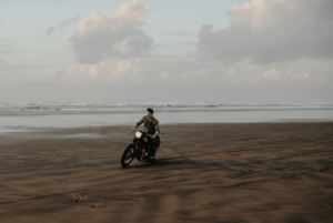 Man riding a motorcycle on the sandy beach at sunset.