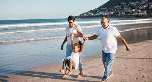 Grandparents hold hands with their granddaughter and swing her in the air by the ocean