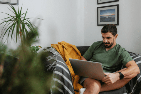 Caucasian Man Using Laptop Sitting In Arm Chair In The Room