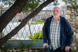 A photo of an older man standing outside with a walker.