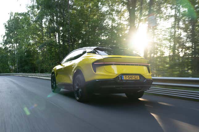 A yellow 2024 Lotus Eletre S SUV drives in a Norwegian forest, rear three-quarter view