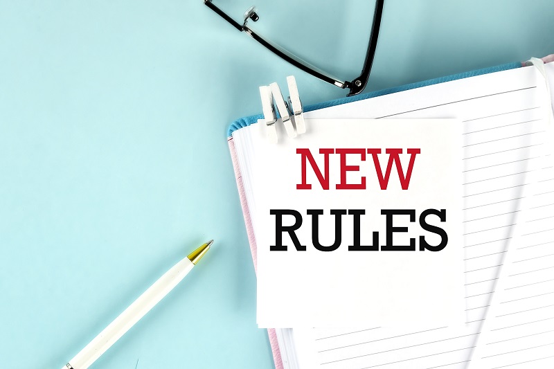 NEW RULES text on a sticky on a notebook with pen and glasses , blue background
