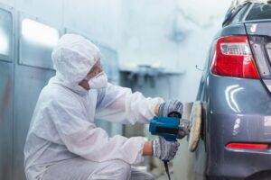 Car repair person buffing out paint after replacing body parts.