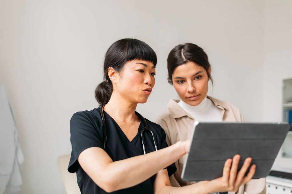 Portrait of beautiful young woman having checkup with her female doctor. Medical doctor showing her test results on digital tablet