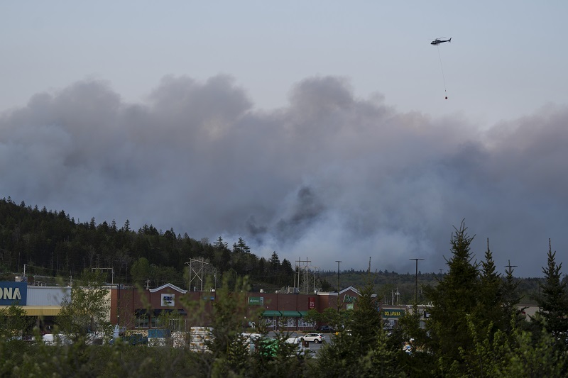 A helicopter carrying water flies over heavy smoke from an out-of-control fire in a suburban community outside of Halifax that spread quickly, engulfing multiple homes and forcing the evacuation of local residents on Sunday May 28,