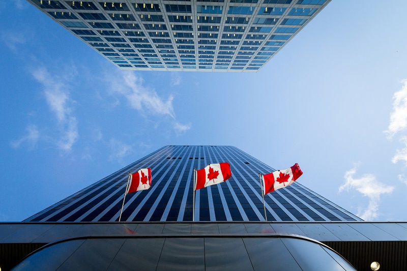 Picture of the canadian flag taken in front of a cold and blue business building.
