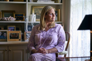 A portrait of a woman at home looking out a window.