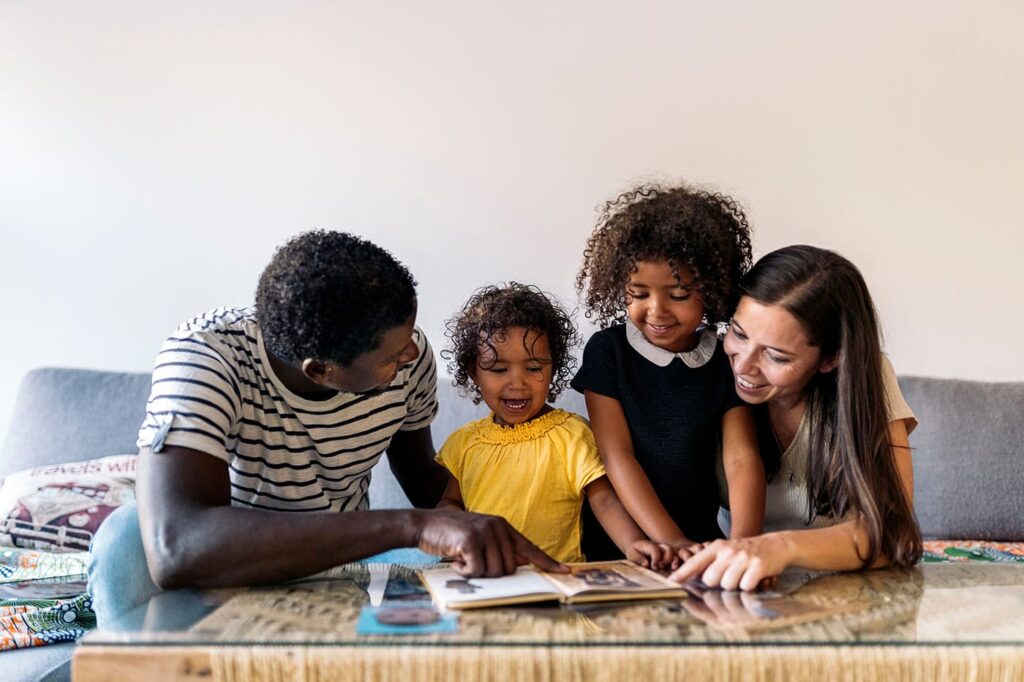 Stock photo of adorable multi-ethnic family reading a book together in the sofa.