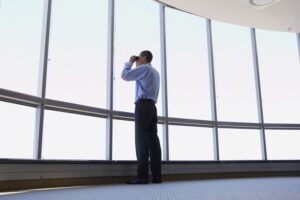 Man looking through binoculars out of office window, low angle view