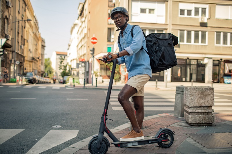 Young African delivery man riding electric scooter and delivering food or packages.