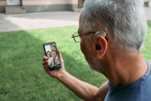 A man with a hearing aid behind the ear communicates with his family via video on his smartphone.