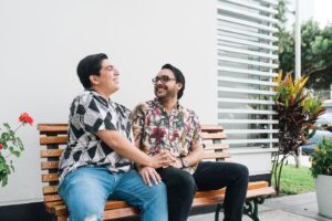 Same-sex couple wearing matching marriage rings, sitting on a bench.