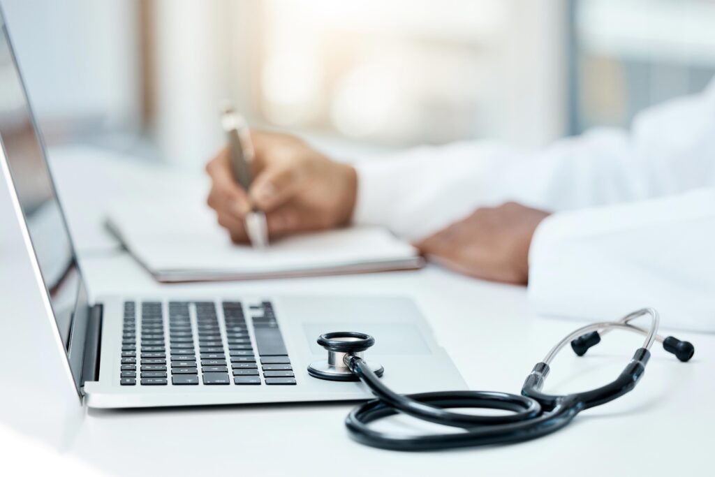 A photo of a doctor taking notes next to a laptop.