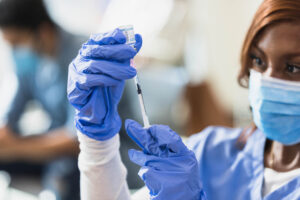 A nurse uses a syringe to pull solution from a vial.