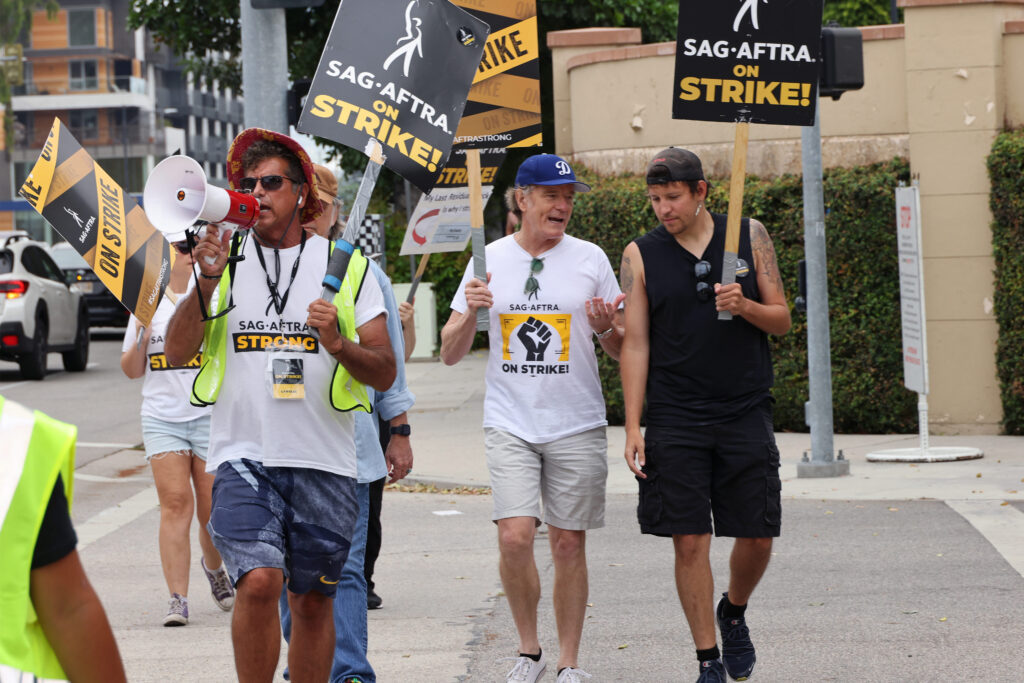 A photo of people walking outside and holding signs that say, "SAG-AFTRA on strike!"