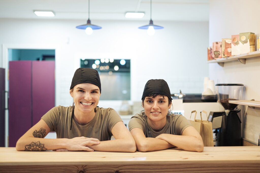 Portrait of two smiling small business owners looking at camera from the restaurant bar