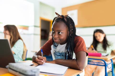 A black teenager smiling while taking notes from the chalkboard. Back to school concept