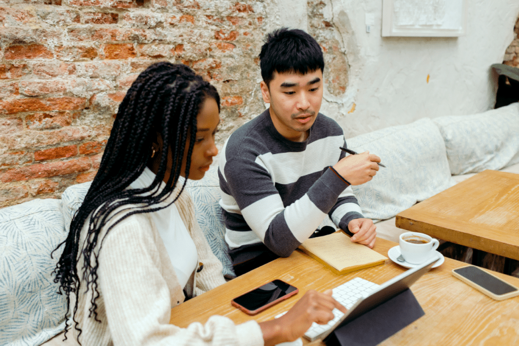 Man and woman sitting by modern co-working space with industrial aesthetic discussing project on tablet device while having coffee