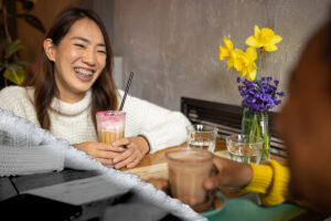 A young woman laughs while enjoying coffee with someone.