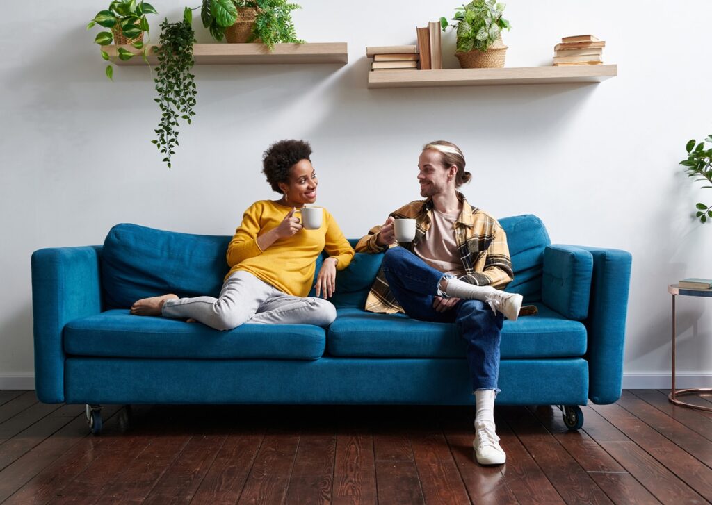 A man and woman sit on a sofa facing each other, touching and talking.