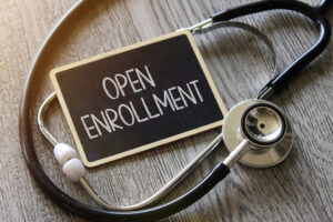 A photo of a chalkboard with "open enrollment" written on it surrounded by a stethoscope.