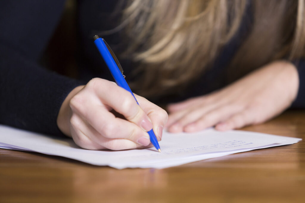 A woman's hand holding a pen and writing on an exam paper