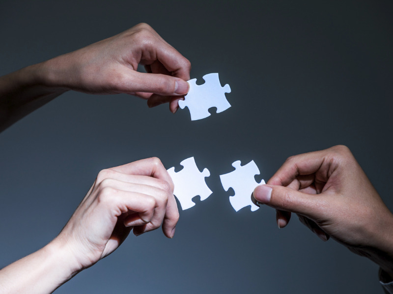 Hands holding jigsaw puzzle pieces to symbolize synergies