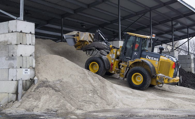 A heavy digger drives up a mound of salt.