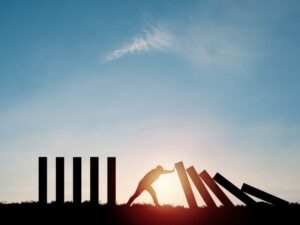 Silhouette of a man pushing rectangle block, which are falling, to stop domino effect