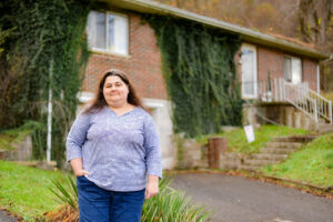 A photo of a woman standing for a portrait outside of her house.