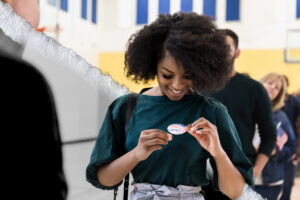 A woman who has just voted places a 'I Voted!' sticker on her shirt.