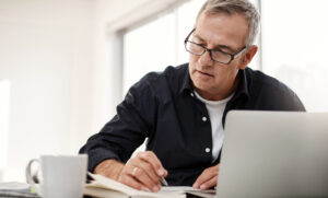 Man on laptop at desk checking papers