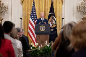 U.S. President Joe Biden is standing at a presidential podium in front of a seated audience in the White House.