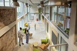 High angle view of female agent standing with prospective buyer in lobby of modern office building and pointing to windows surrounding second floor.